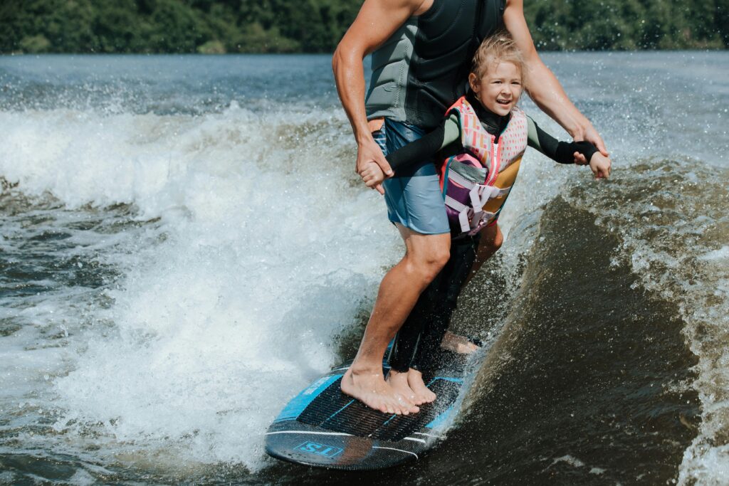 A father and daughter enjoying a thrilling wake surfing experience on a sunny day.
